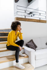 Pensive young woman sitting on stairs at home - GIOF08258