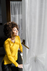 Portrait of happy young woman standing at open window looking up - GIOF08262