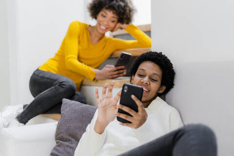 Zwei junge Frauen entspannen sich zu Hause und benutzen ihre Smartphones, lizenzfreies Stockfoto