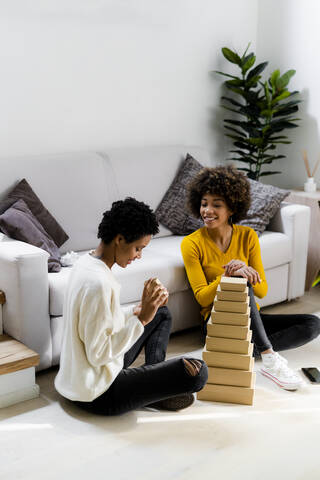 Zwei junge Frauen sitzen zu Hause auf dem Boden und stapeln Kisten im Wohnzimmer, lizenzfreies Stockfoto