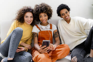 Gruppenbild von drei Freunden, die mit einem Smartphone auf einer Couch sitzen - GIOF08303