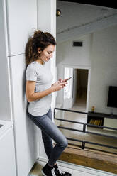 Smiling young woman using smartphone at home - GIOF08331