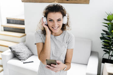Portrait of smiling young woman listening music with headphones and cell phone - GIOF08334