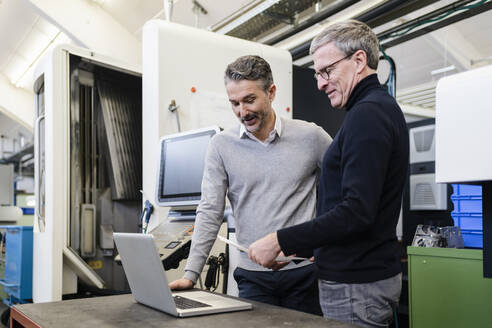 Männliche Vorgesetzte diskutieren in einer Fabrik über einen Laptop - DIGF12616