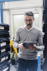 Älterer männlicher Vorgesetzter, der ein digitales Tablet in einer Fabrik benutzt - DIGF12630