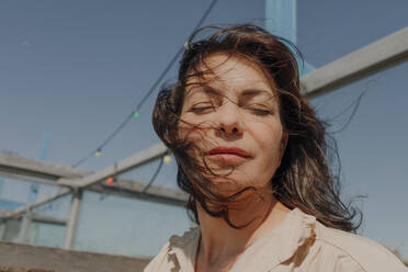 Frau mit zerzaustem Haar und geschlossenen Augen gegen den Himmel an einem sonnigen Tag - OGF00429
