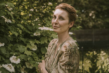 Mid adult woman standing by flowering plant at garden - MFF05854