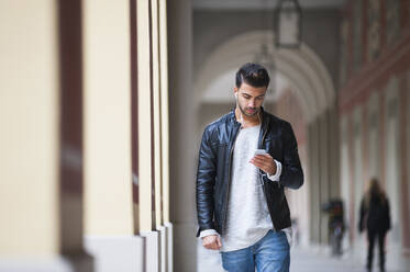 Junger Mann, der ein Smartphone benutzt, während er durch einen Korridor geht - DIGF12642