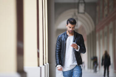 Young man using smart phone while walking in corridor - DIGF12642
