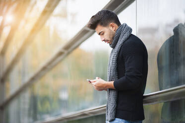 Mann benutzt Smartphone, während er an der Wand steht - DIGF12646