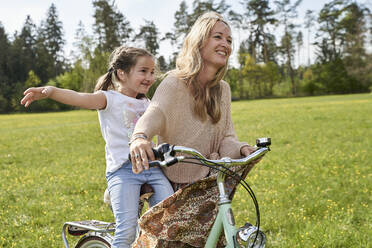Girl with arms outstretched enjoying bicycle ride with mother on plants - AUF00515