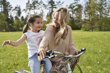 Smiling blond woman looking at daughter enjoying bicycle ride with arms outstretched - AUF00516