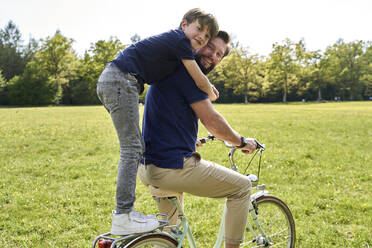 Glücklicher Junge, der seinen Vater umarmt, während er eine Fahrradtour an einem sonnigen Tag genießt - AUF00517