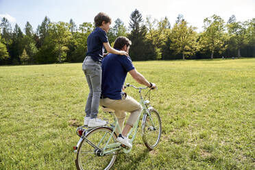 Vater und Sohn genießen eine Fahrradtour im Gras an einem sonnigen Tag - AUF00518