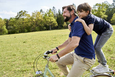 Glücklicher Vater und Sohn genießen die Fahrradtour im Gras an einem sonnigen Tag - AUF00520