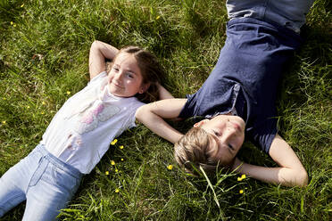 Lächelndes Mädchen liegt neben ihrem Bruder im Gras an einem sonnigen Tag - AUF00522