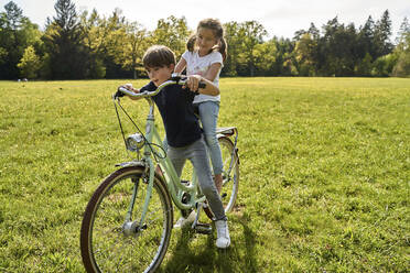 Geschwister genießen eine Fahrradtour im Gras an einem sonnigen Tag - AUF00531