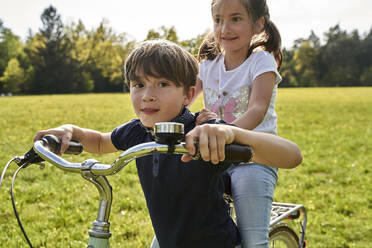 Junge, der seine Schwester auf dem Fahrrad mitnimmt, an einem sonnigen Tag - AUF00532