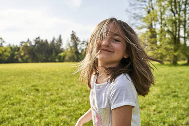 Verspieltes Mädchen mit zerzaustem Haar im Gras stehend an einem sonnigen Tag - AUF00536