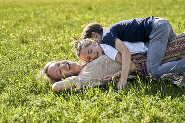 Fröhliche Frau mit Kindern auf ihr liegend an einem sonnigen Tag - AUF00538
