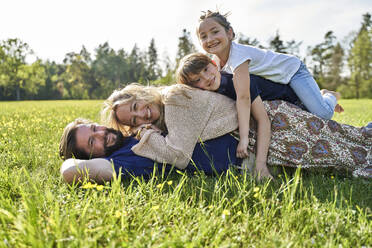 Glückliche Familie im Gras liegend an einem sonnigen Tag - AUF00539