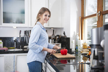 Smiling beautiful woman cutting red bell pepper at kitchen counter - DIGF12657