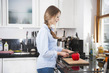 Junge Frau schneidet rote Paprika am Küchentisch - DIGF12664