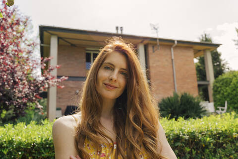 Young woman with long brown hair standing in garden on sunny day stock photo