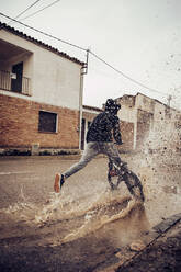 Jugendlicher, der beim Radfahren auf der Straße Wasser in eine Pfütze spritzt - ACPF00730
