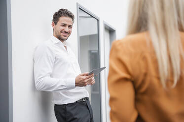 Confident businessman holding digital tablet while looking at female colleague in office - DIGF12691