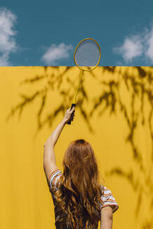 Frau hält Badmintonschläger über gelbe Wand während sonnigen Tag - AFVF06445