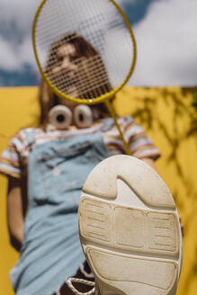 Junge Frau hält Badmintonschläger mit Schuhsohle im Vordergrund an einem sonnigen Tag - AFVF06448