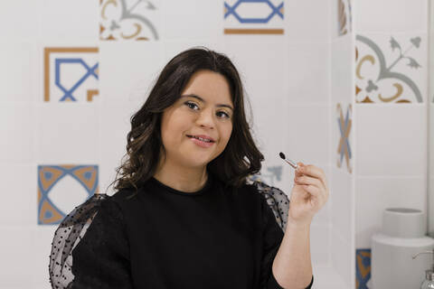 Confident woman with down syndrome holding make-up brush in bathroom at home stock photo
