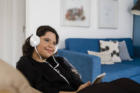 Nachdenkliche Frau mit Down-Syndrom hört Musik und entspannt sich im Wohnzimmer - DCRF00221
