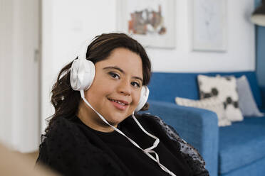 Happy woman with down syndrome listening music while relaxing in living room - DCRF00222