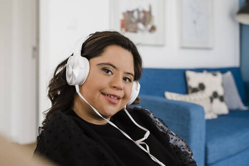 Glückliche Frau mit Down-Syndrom hört Musik und entspannt sich im Wohnzimmer - DCRF00222