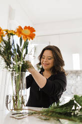 Happy young woman with down syndrome arranging flowers in vase on table at home - DCRF00227