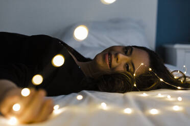 Glückliche junge Frau mit Down-Syndrom liegt auf einem beleuchteten Bett zu Hause - DCRF00244