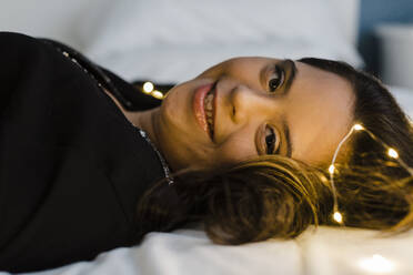 Lächelnde junge Frau mit Down-Syndrom auf beleuchtetem Bett zu Hause liegend - DCRF00245