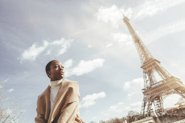 Nachdenkliche junge Frau mit Eiffelturm im Hintergrund an einem sonnigen Tag, Paris, Frankreich - KIJF03049
