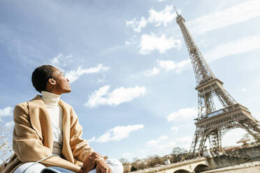 Junge Frau betrachtet den Eiffelturm gegen den Himmel an einem sonnigen Tag, Paris, Frankreich - KIJF03050