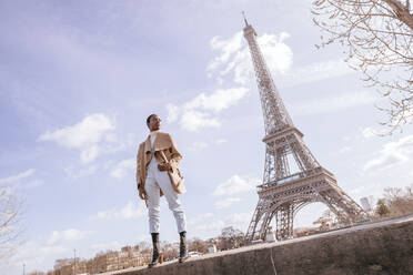 Nachdenkliche junge Frau steht auf einer Stützmauer mit dem Eiffelturm im Hintergrund, Paris, Frankreich - KIJF03052