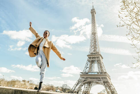 Excited woman jumping from retaining wall with Eiffel Tower in background, Paris, France - KIJF03053