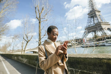 Frau mit Smartphone auf Brücke mit Eiffelturm im Hintergrund gegen den Himmel, Paris, Frankreich - KIJF03061