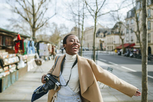 Cheerful woman holding DSLR camera on sidewalk in Paris, France - KIJF03064