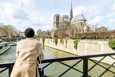 Frau betrachtet Notre Dame de Paris von einer Brücke aus gegen den Himmel, Paris, Frankreich - KIJF03066