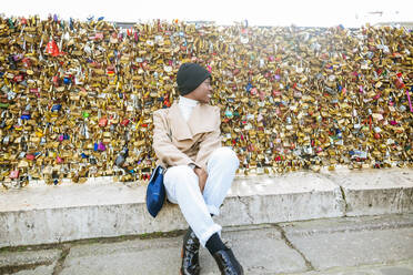 Junge Frau sitzt gegen Liebesschlösser auf einer Brücke, Paris, Frankreich - KIJF03069