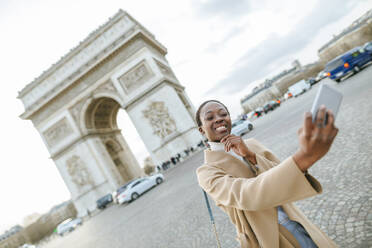 Glückliche junge Frau, die ein Selfie vor dem Arc de Triomphe macht, Paris, Frankreich - KIJF03078