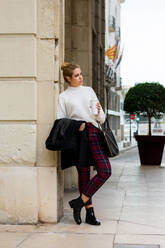 Young woman drinks coffee and looks around her on the street - CAVF83651