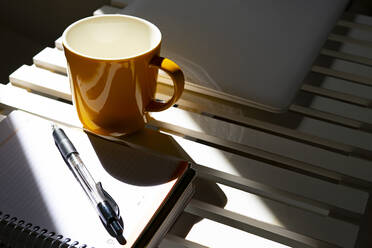 Gelbe Tasse Kaffee auf einem Schreibtisch mit einem Kalender und einem Stift. - CAVF83660